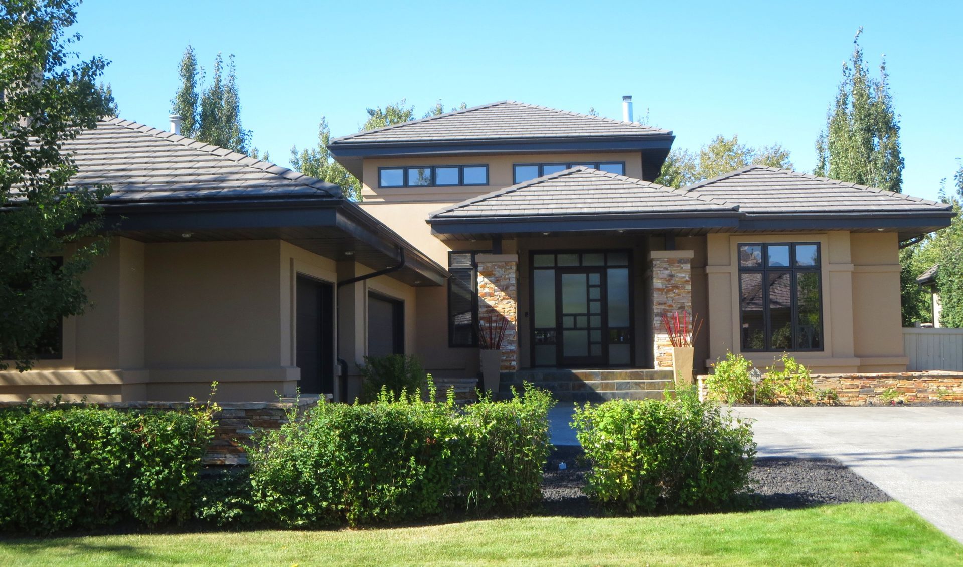 Tan stucco house with dark roof and trim, stone accents, and manicured front yard.