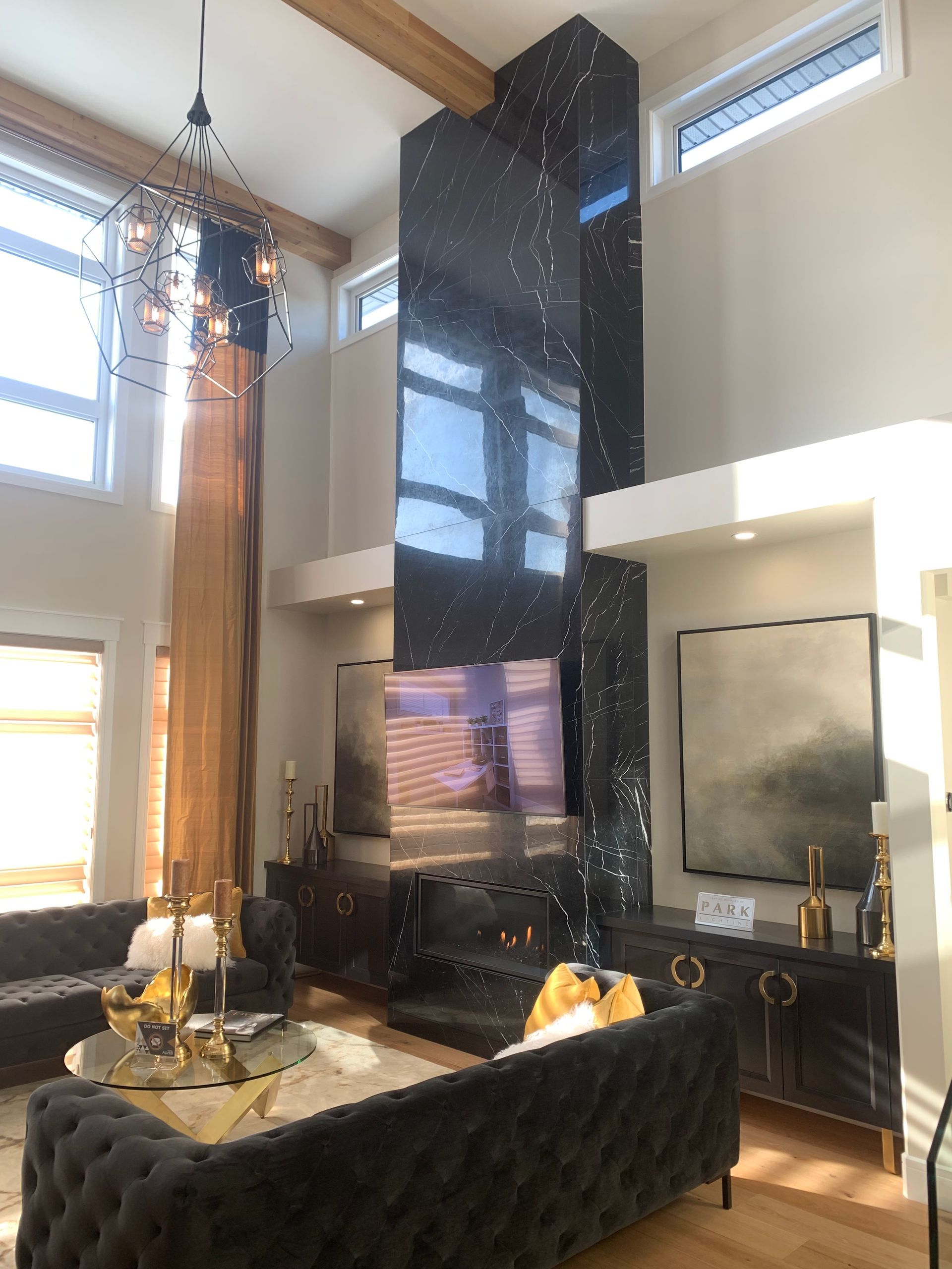 Living room with a tall, black star-studded fireplace, black sofas, and a large chandelier.