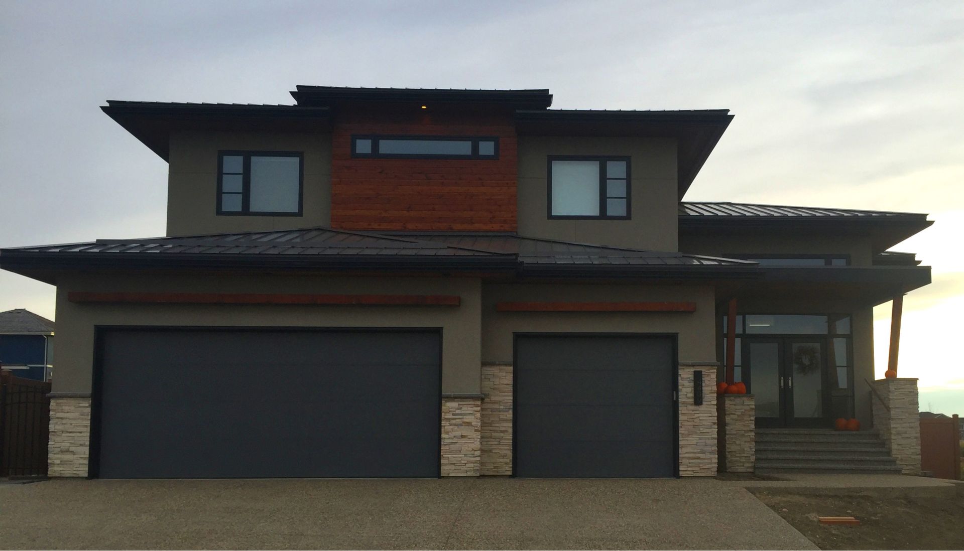 Modern two-story house with gray exterior, dark garage doors, and wood accents.