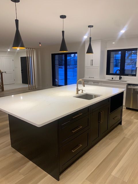 Modern kitchen with island and pendant lights. Black cabinets, white countertop, and wood floors.