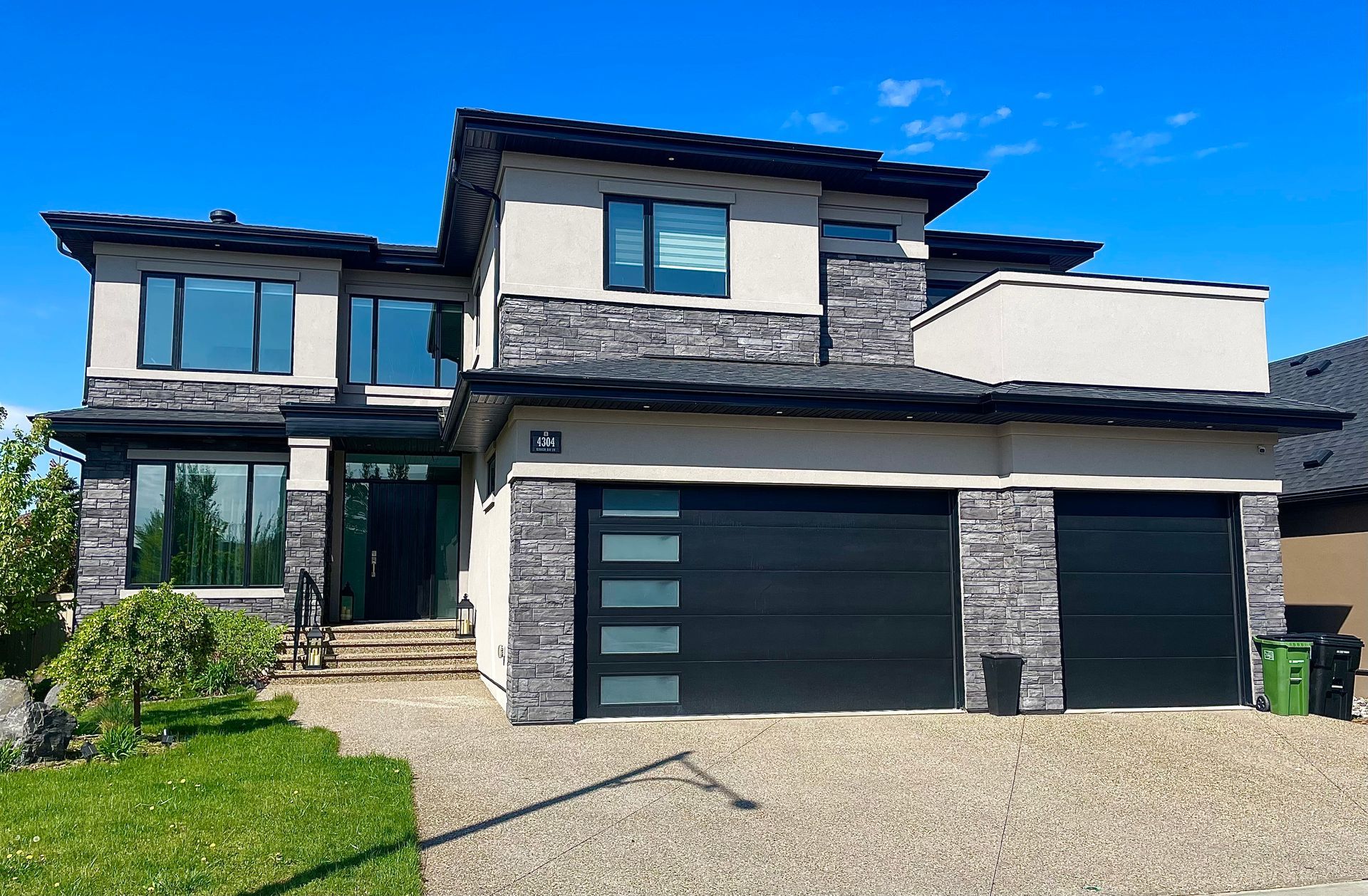 Two-story modern house with black garage doors, stone accents, and blue sky.