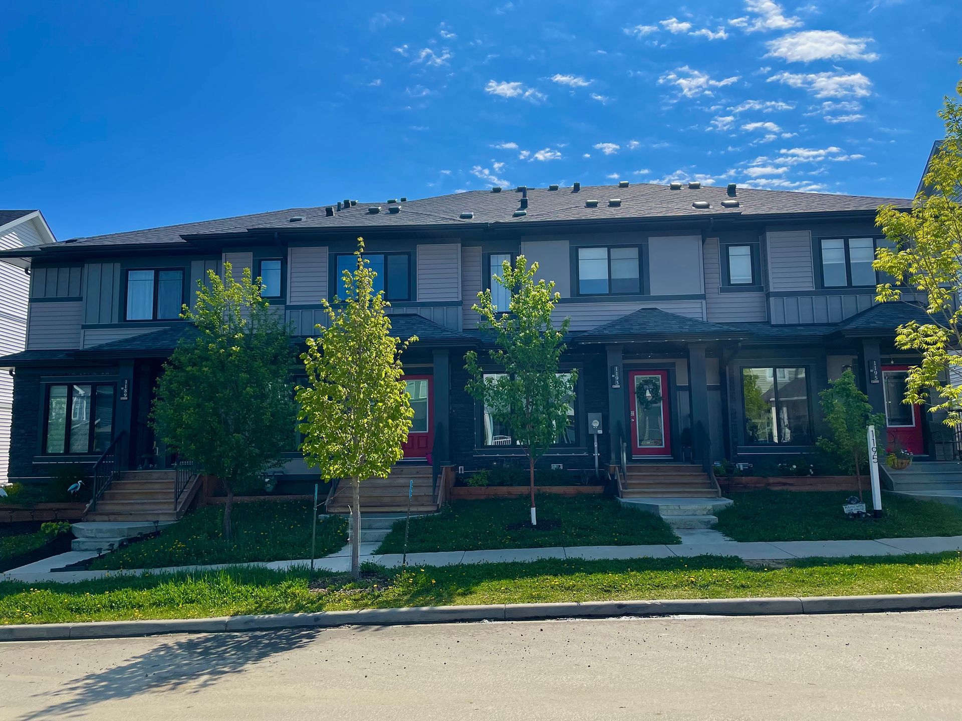 Row of modern townhouses with red doors and small trees in front, under a blue sky.