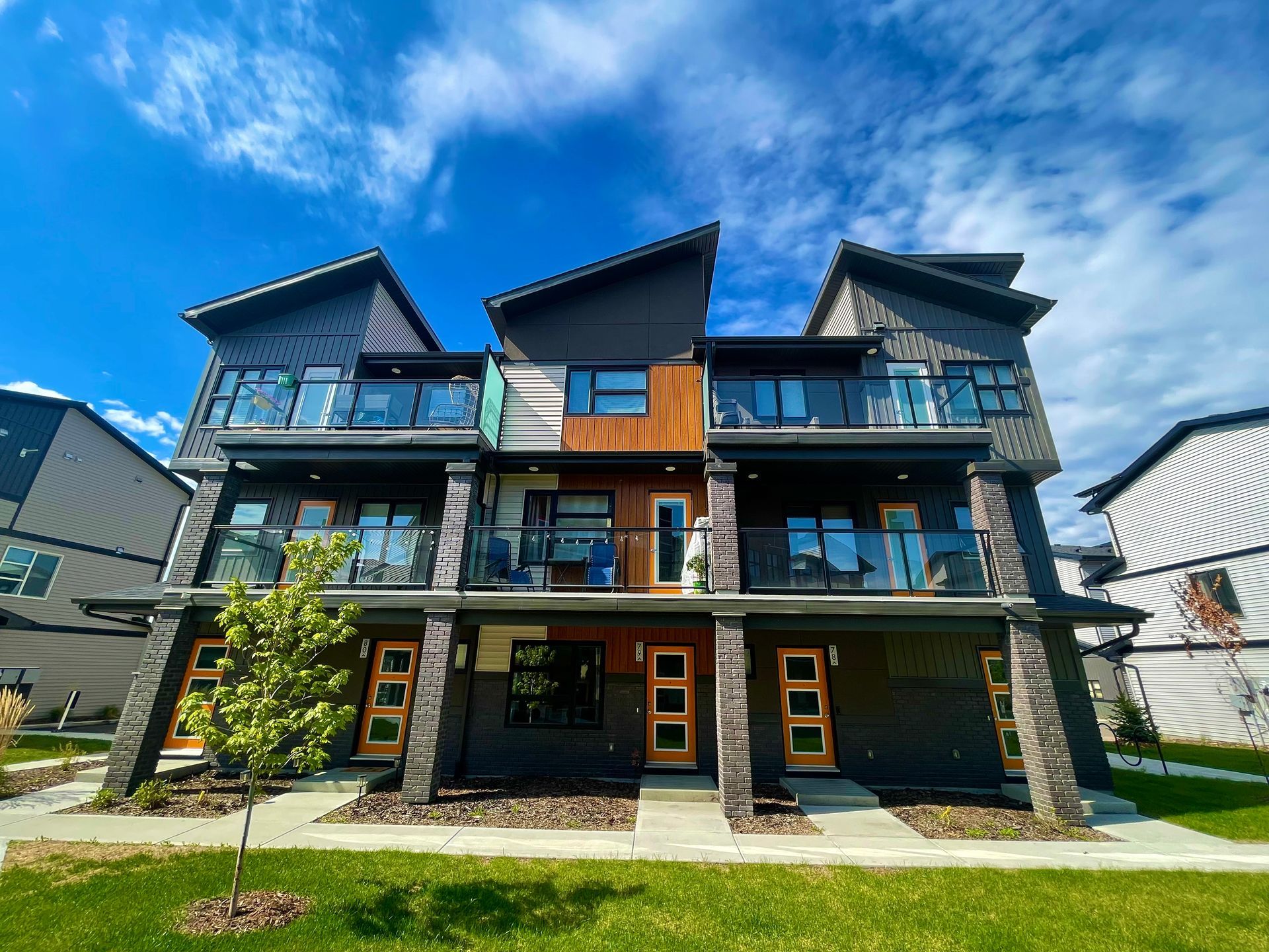 Modern townhomes with balconies and contrasting dark and wood-toned exterior, under a blue sky.
