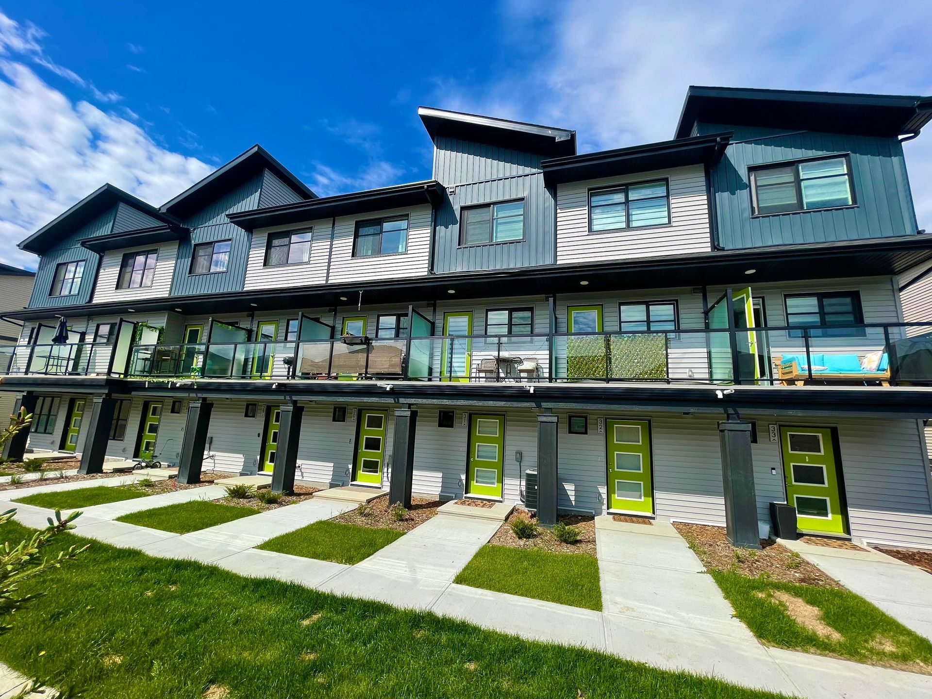 Row of modern townhouses with turquoise and green accents and individual entryways.