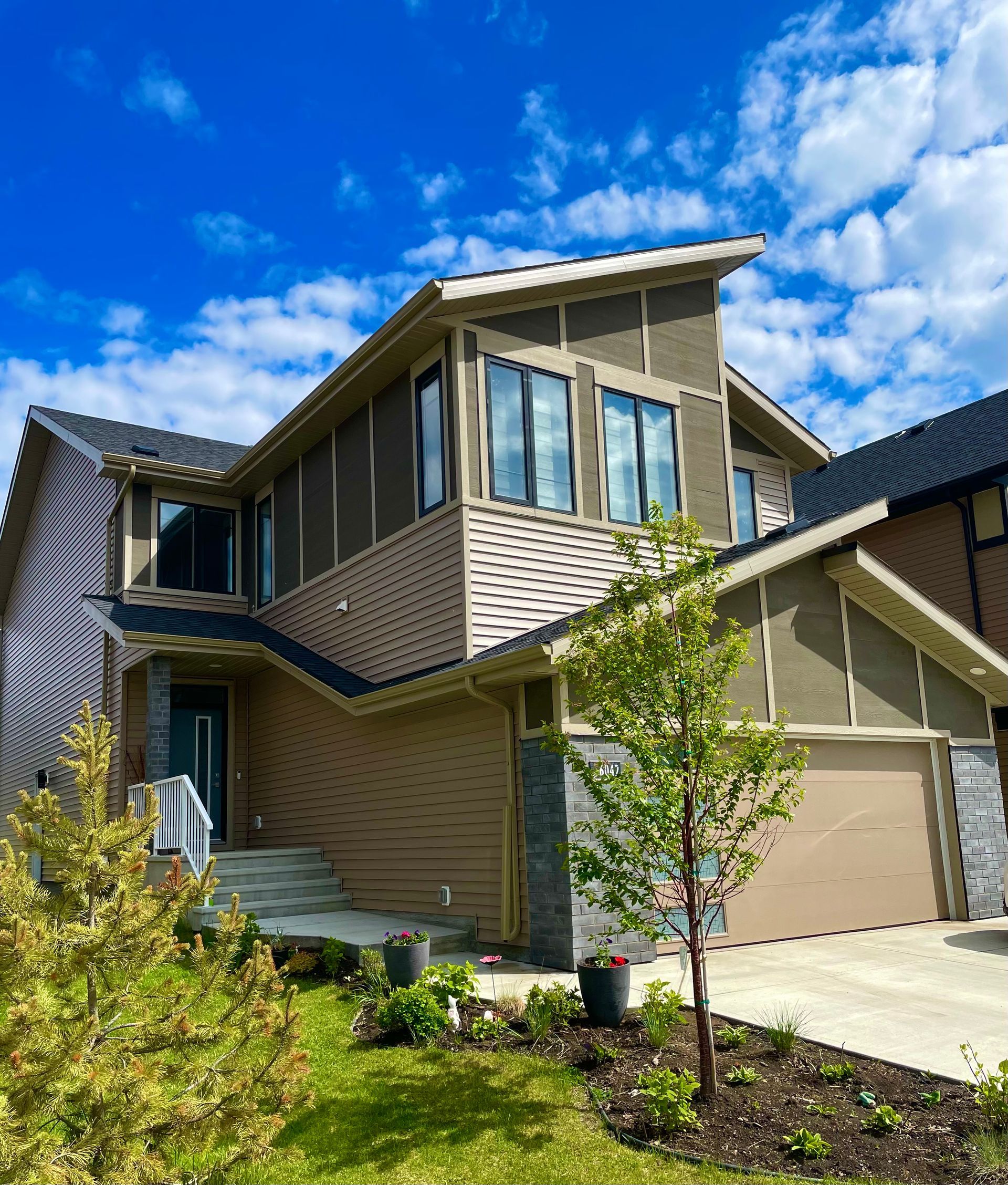 Two-story house with brown siding, stone accents, garage, and blue sky.