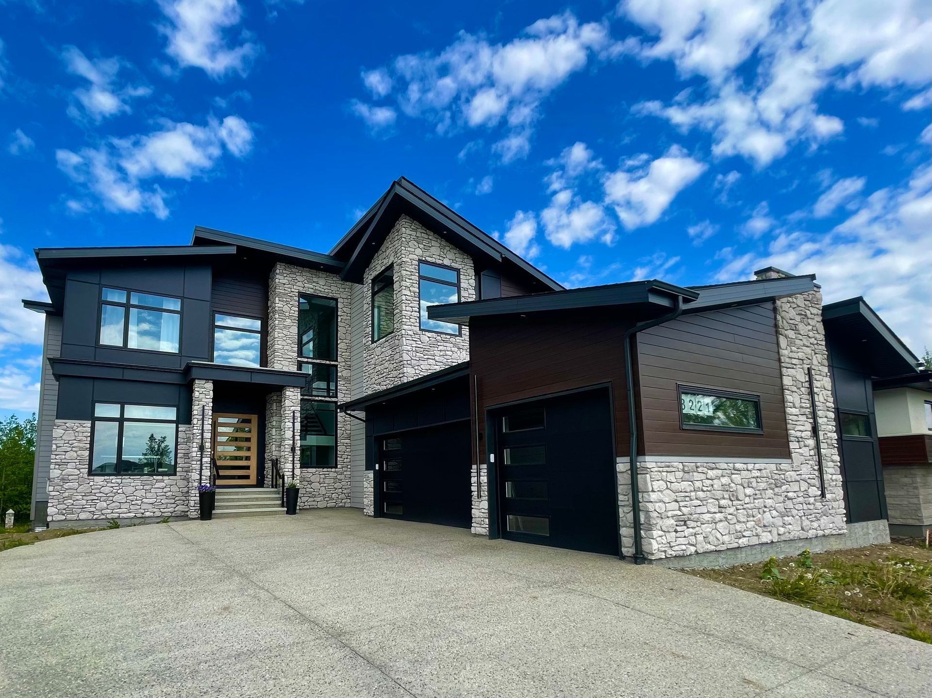 Modern two-story house with stone and dark siding, black garage doors, and blue sky.