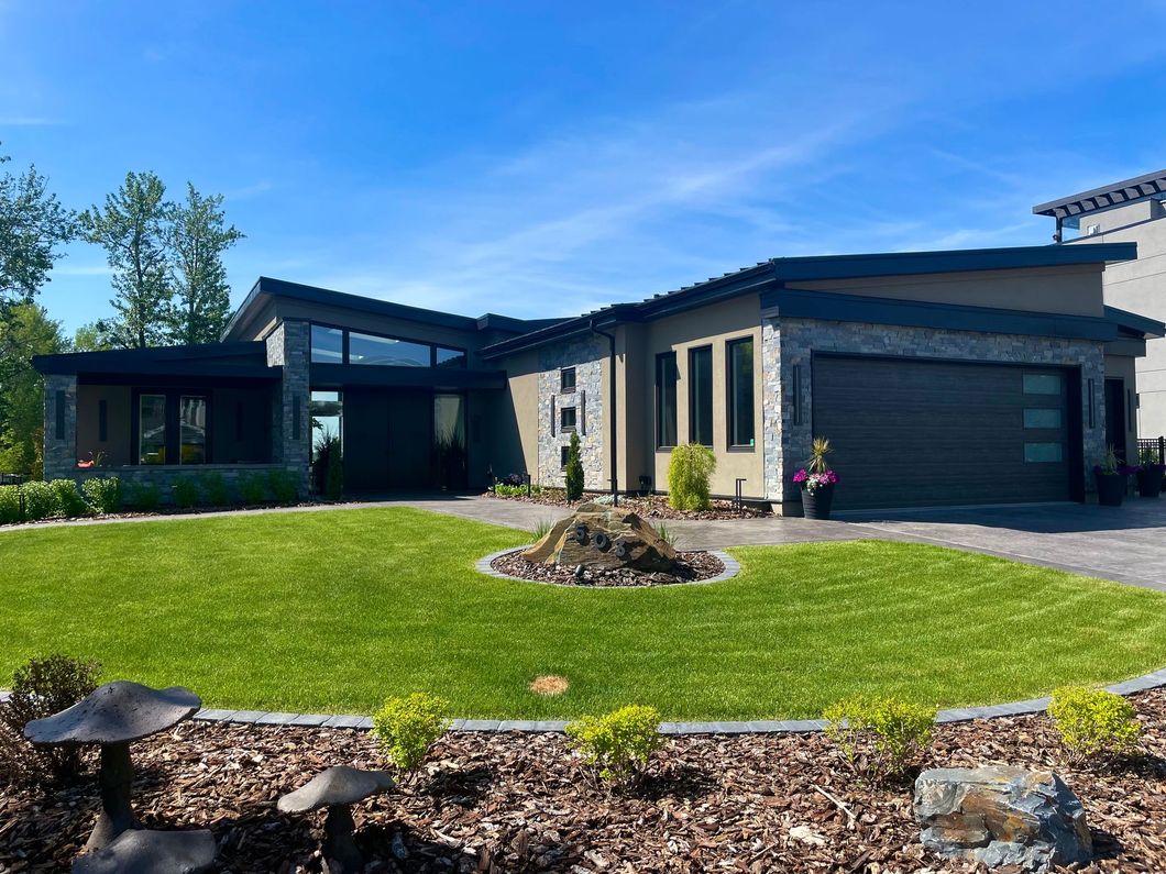 Modern, single-story house with stone and dark siding, manicured lawn, and blue sky.