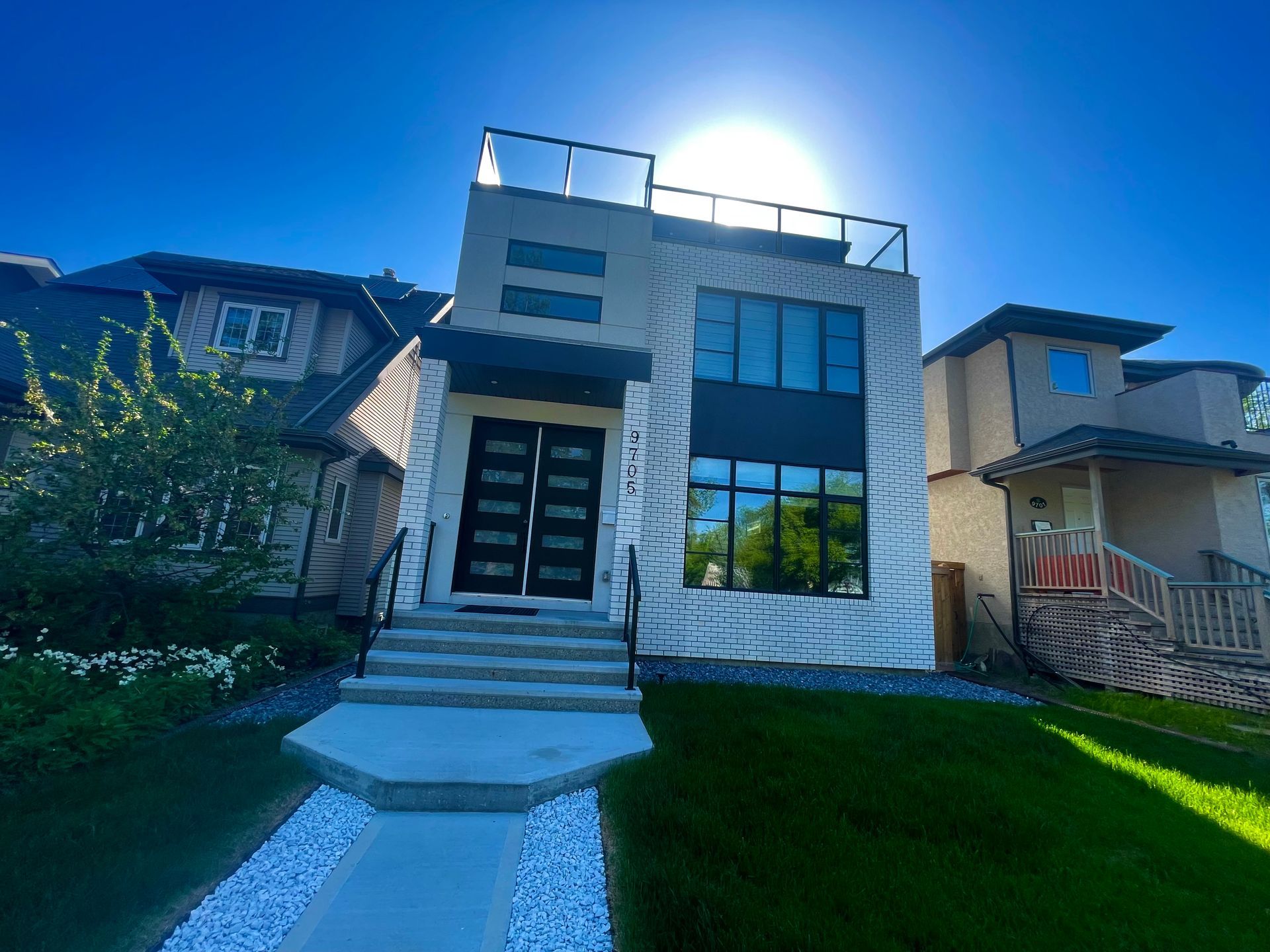 Modern two-story house with glass windows and a rooftop deck on a sunny day.