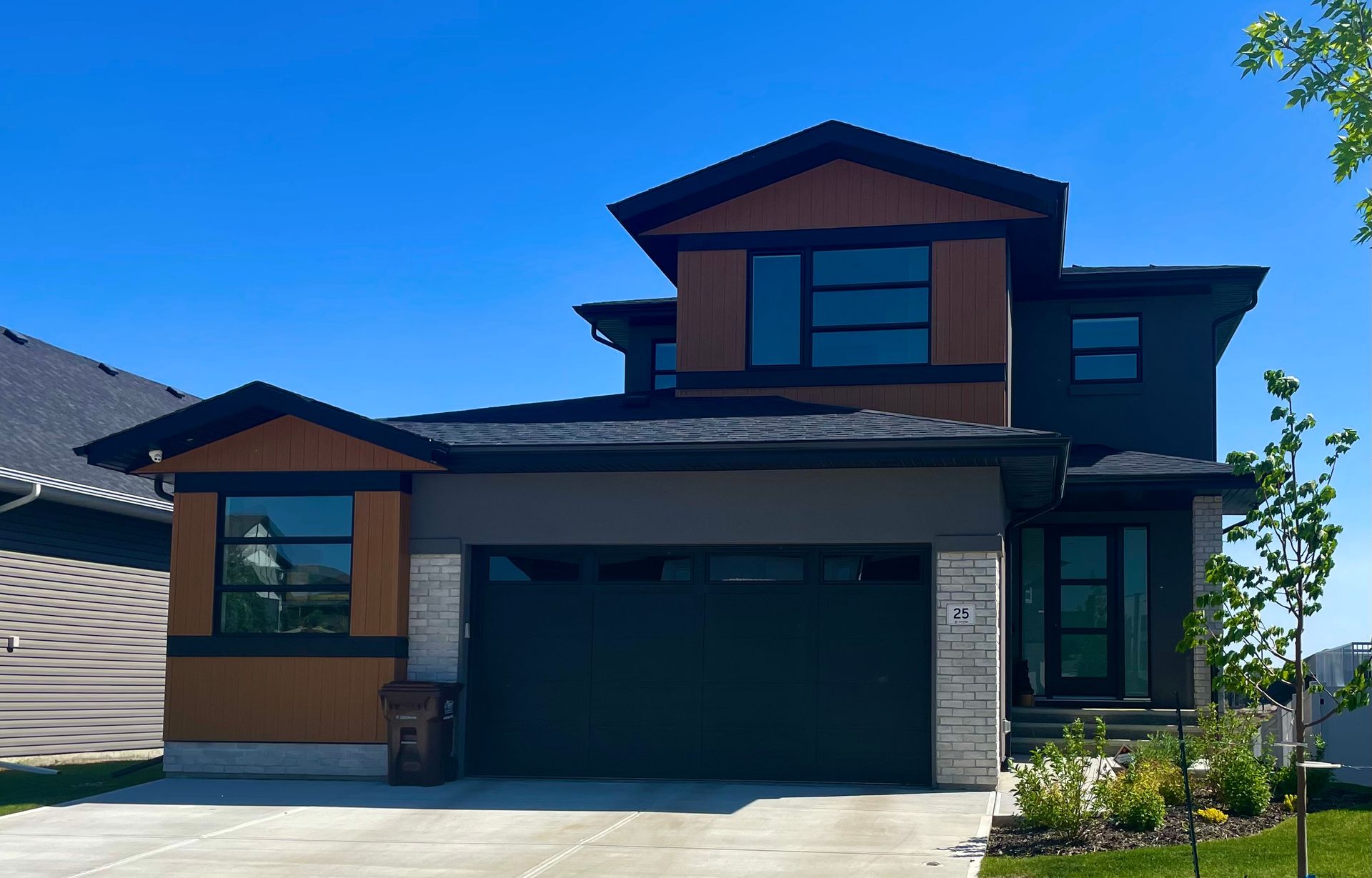 Modern two-story house with brown, gray, and black exterior. Blue sky backdrop.