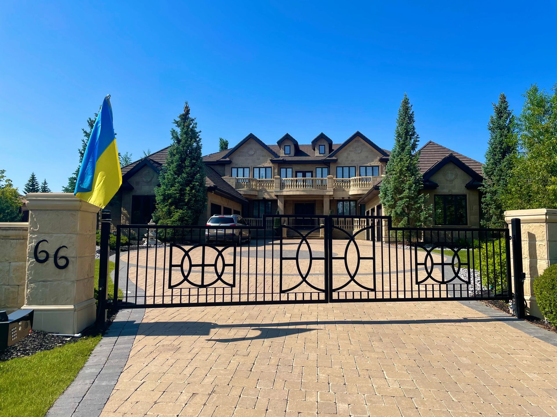 Large house behind a black gate with a Ukrainian flag, under a blue sky.