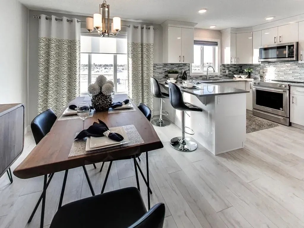Dining area with wooden table, modern chairs, open to a white kitchen.