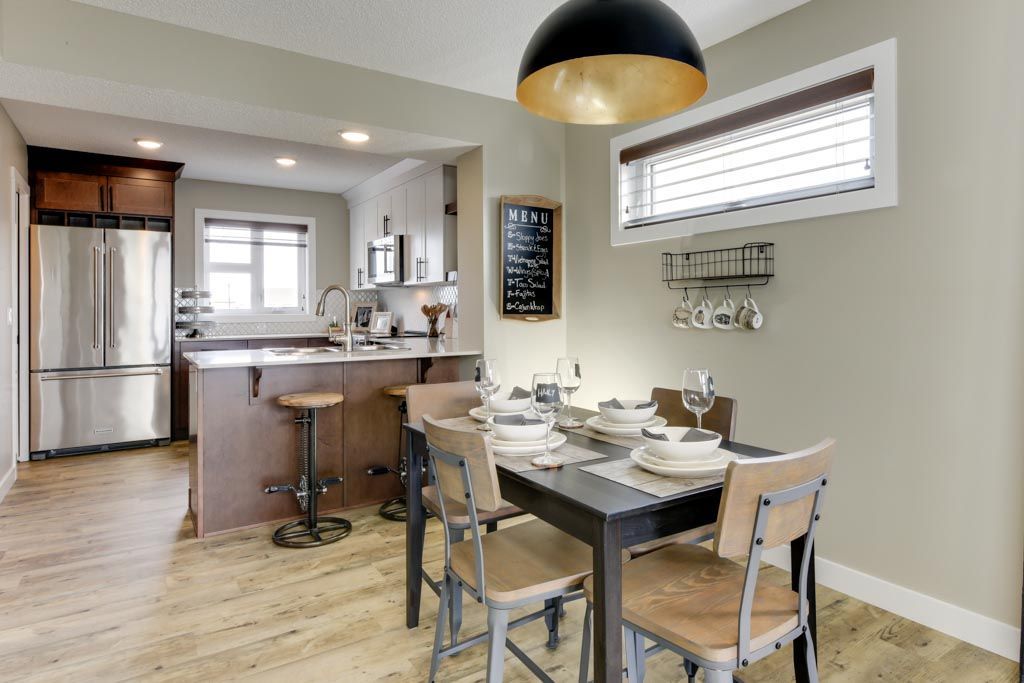 Dining room with table and chairs, open to kitchen with stainless steel appliances, light wood floors, and a black and gold pendant lamp.