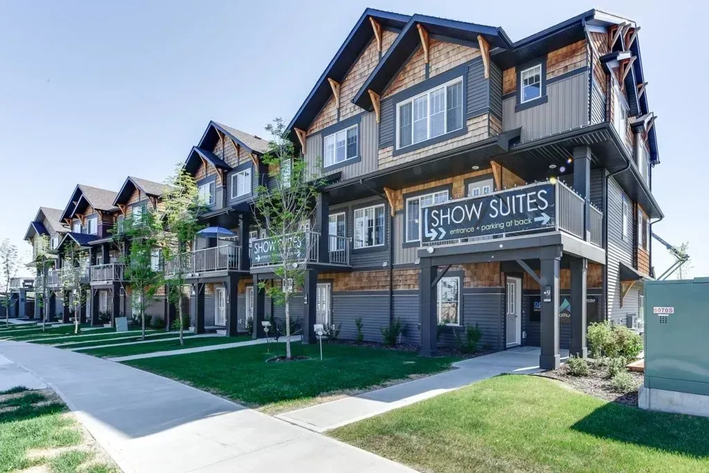 Row of Flow Suites apartments with brown and gray exteriors, sidewalk, green grass, and clear sky.