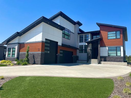 Modern two-story house with gray, white, and brown exterior. Black trim and garage door. Sunny day with green grass.