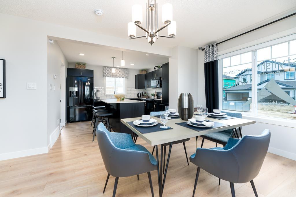 Dining room with table and chairs open to a kitchen. Light wood floors, modern decor, and large windows.