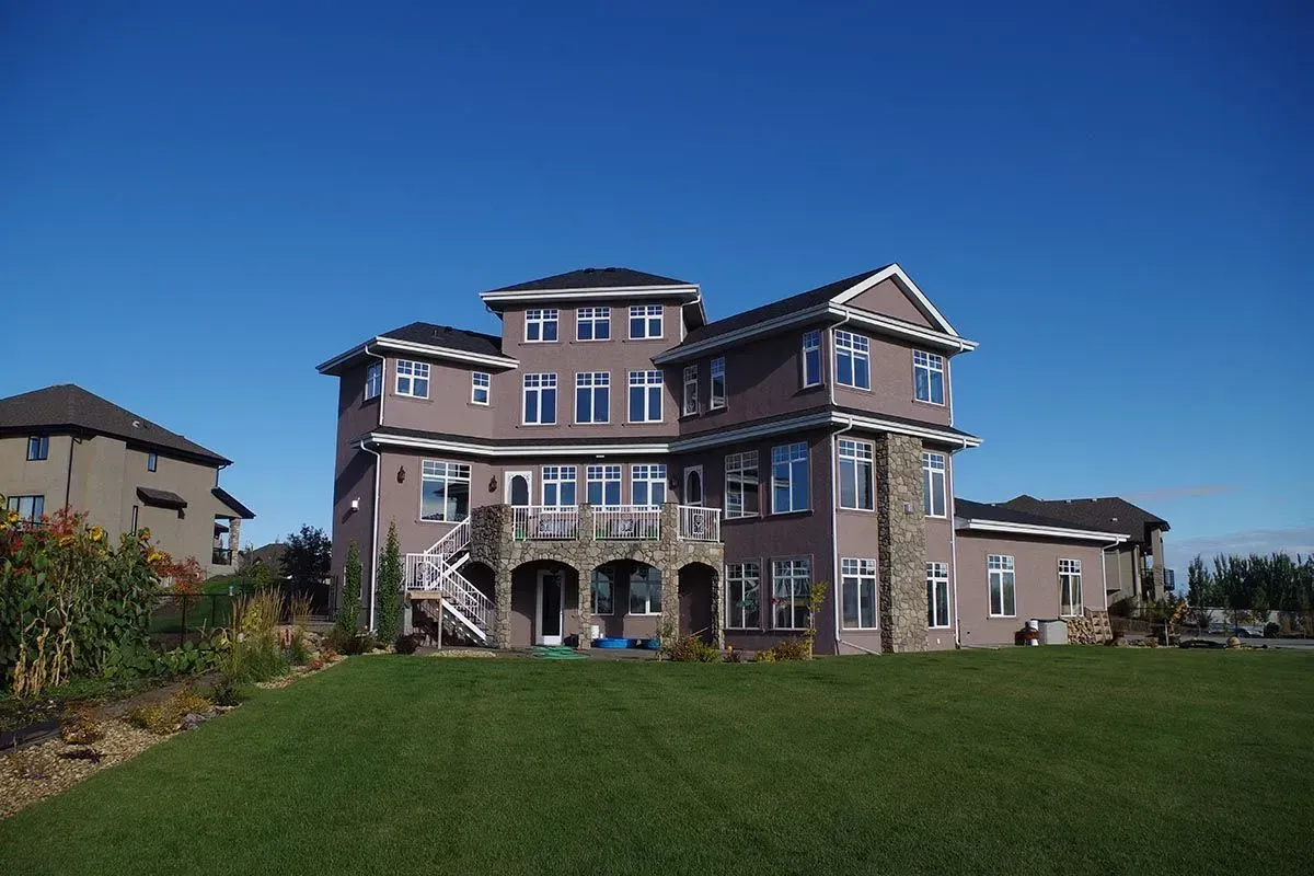 Large, multi-story house with a purple exterior, arched entrance, and green lawn under a blue sky.
