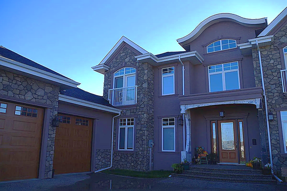Two-story house with stone and purple stucco exterior; brown garage door, blue sky.