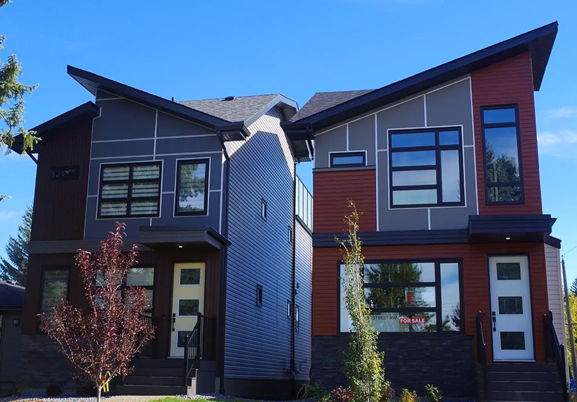 Modern duplex with dark grey and red siding, dark trim, and large windows against a blue sky.