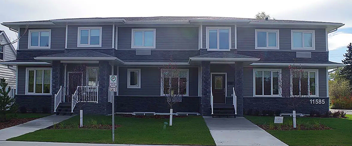 Two-story gray townhouses with green lawn and sidewalk.