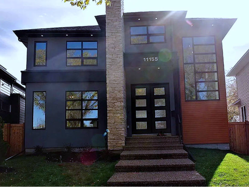 Modern two-story house with gray and wood siding, black-framed windows, and stone chimney. Steps lead to the front door.