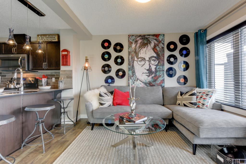 Living room with gray sectional sofa, record wall, and John Lennon portrait.