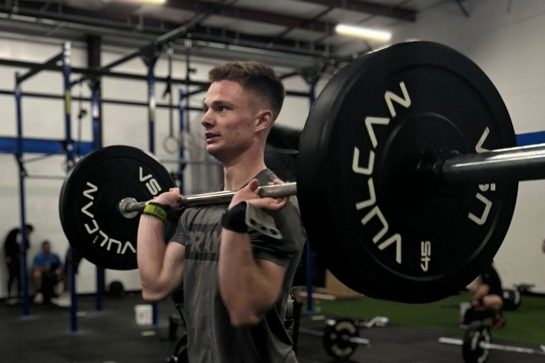 A woman is squatting with a barbell over her head in a gym.