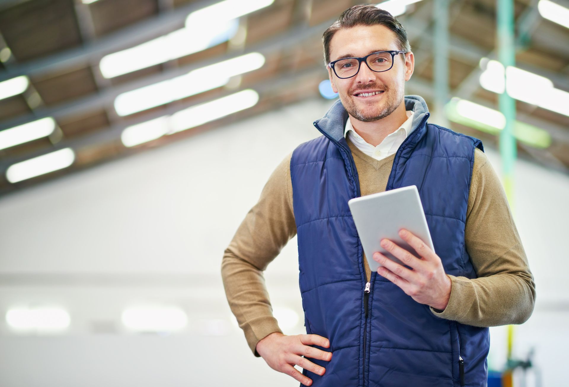 A man in a vest is holding a tablet in a warehouse.
