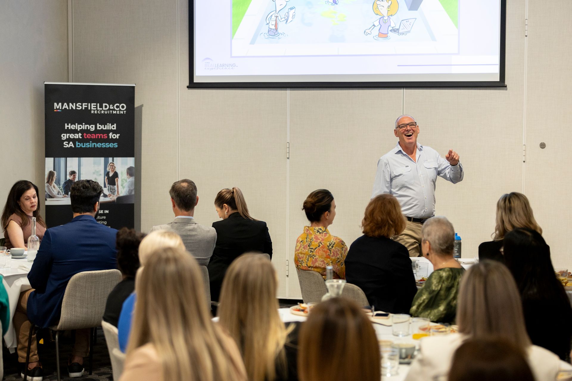 A man is giving a presentation to a group of people sitting at tables.
