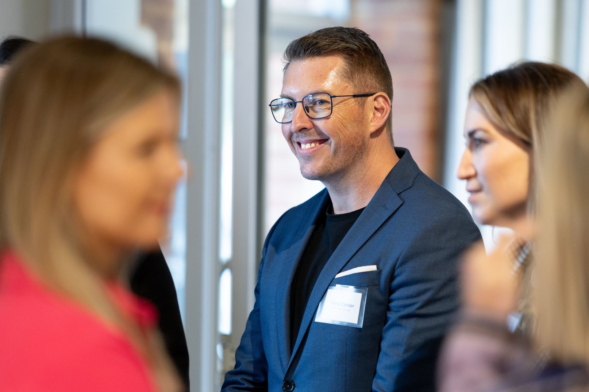 A man in a suit and glasses is smiling while talking to two women.