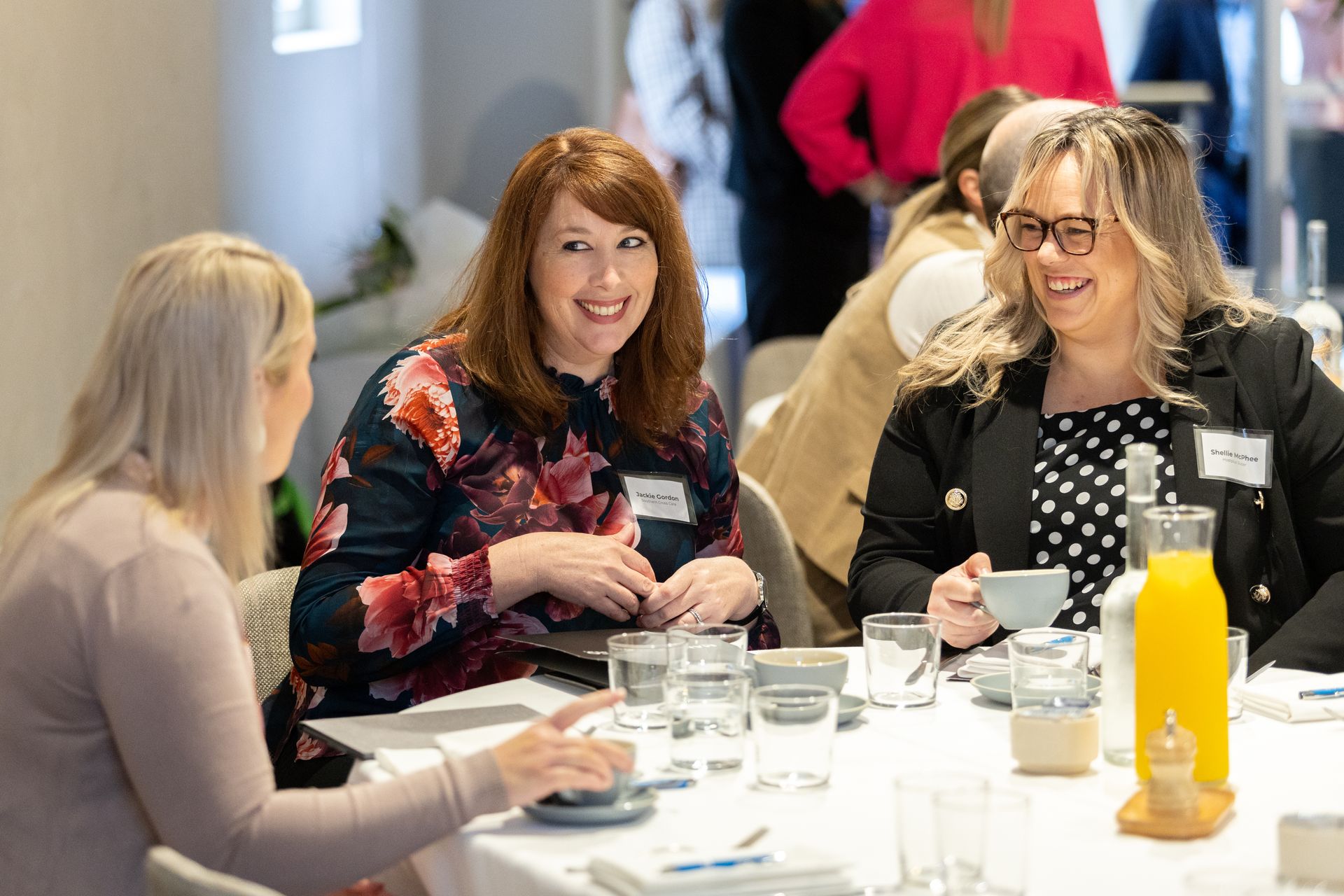 A group of women are sitting at a table talking to each other.