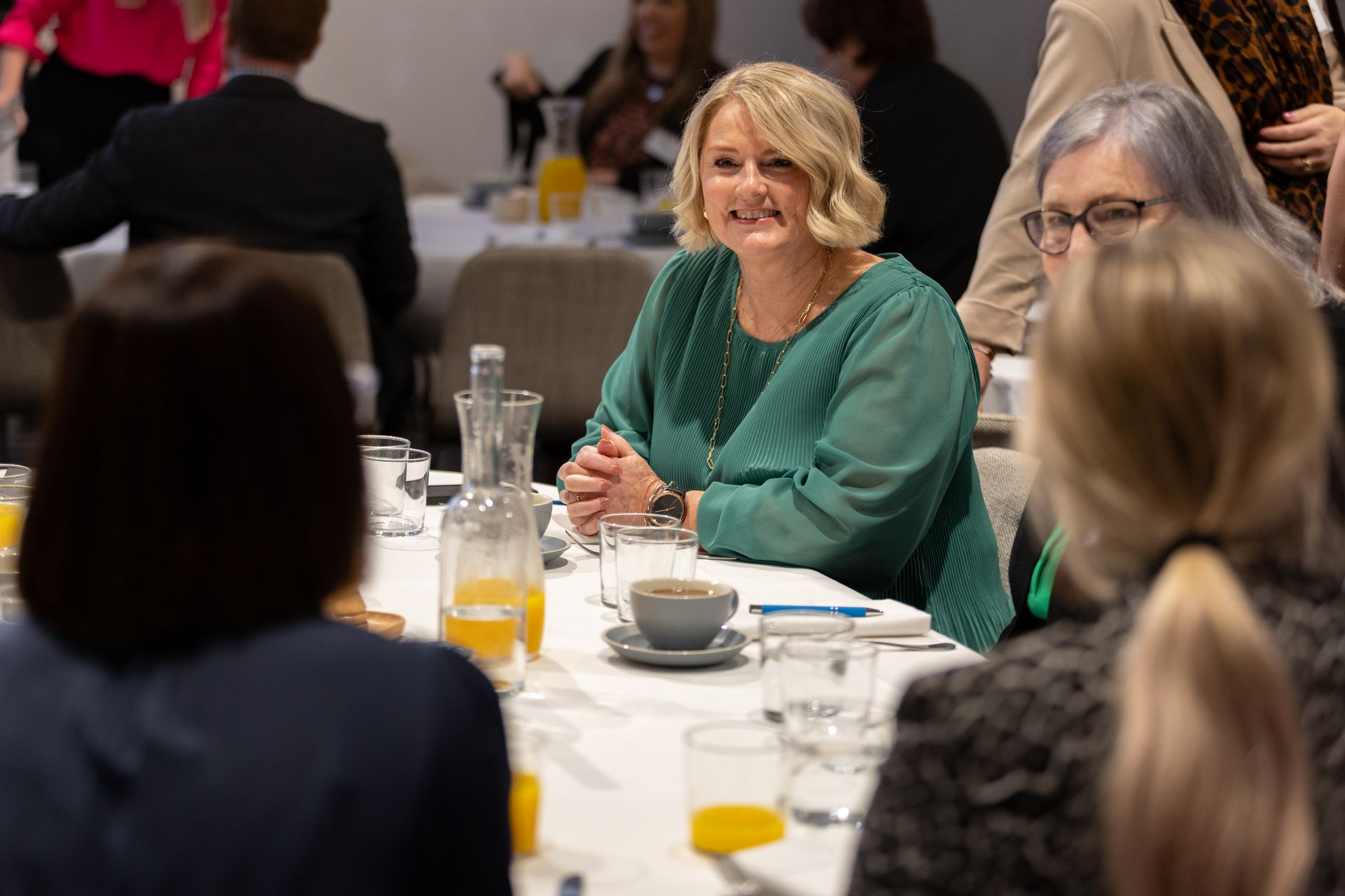 A woman in a green shirt is sitting at a table with other people.