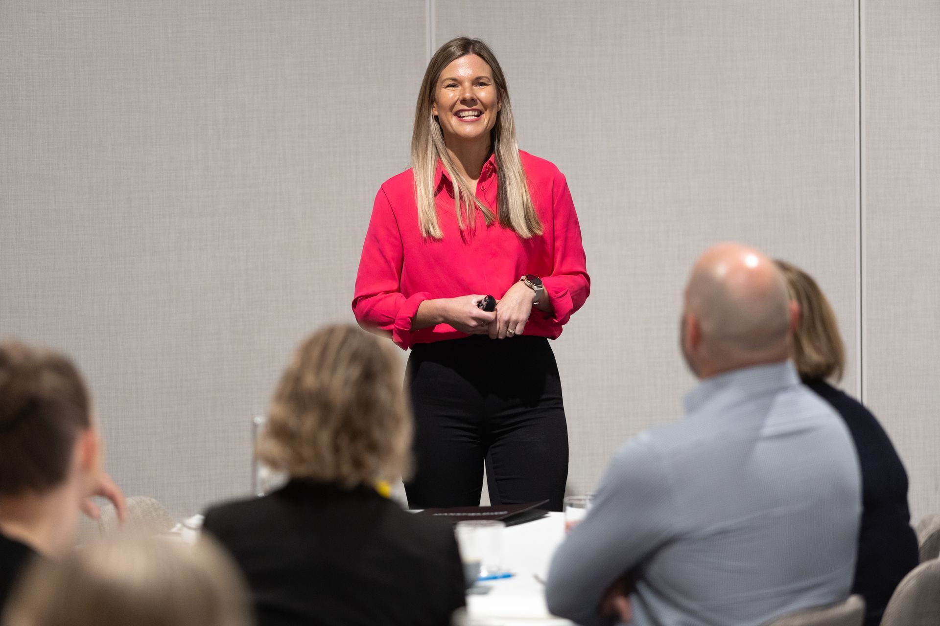 A woman in a pink shirt is giving a presentation to a group of people.