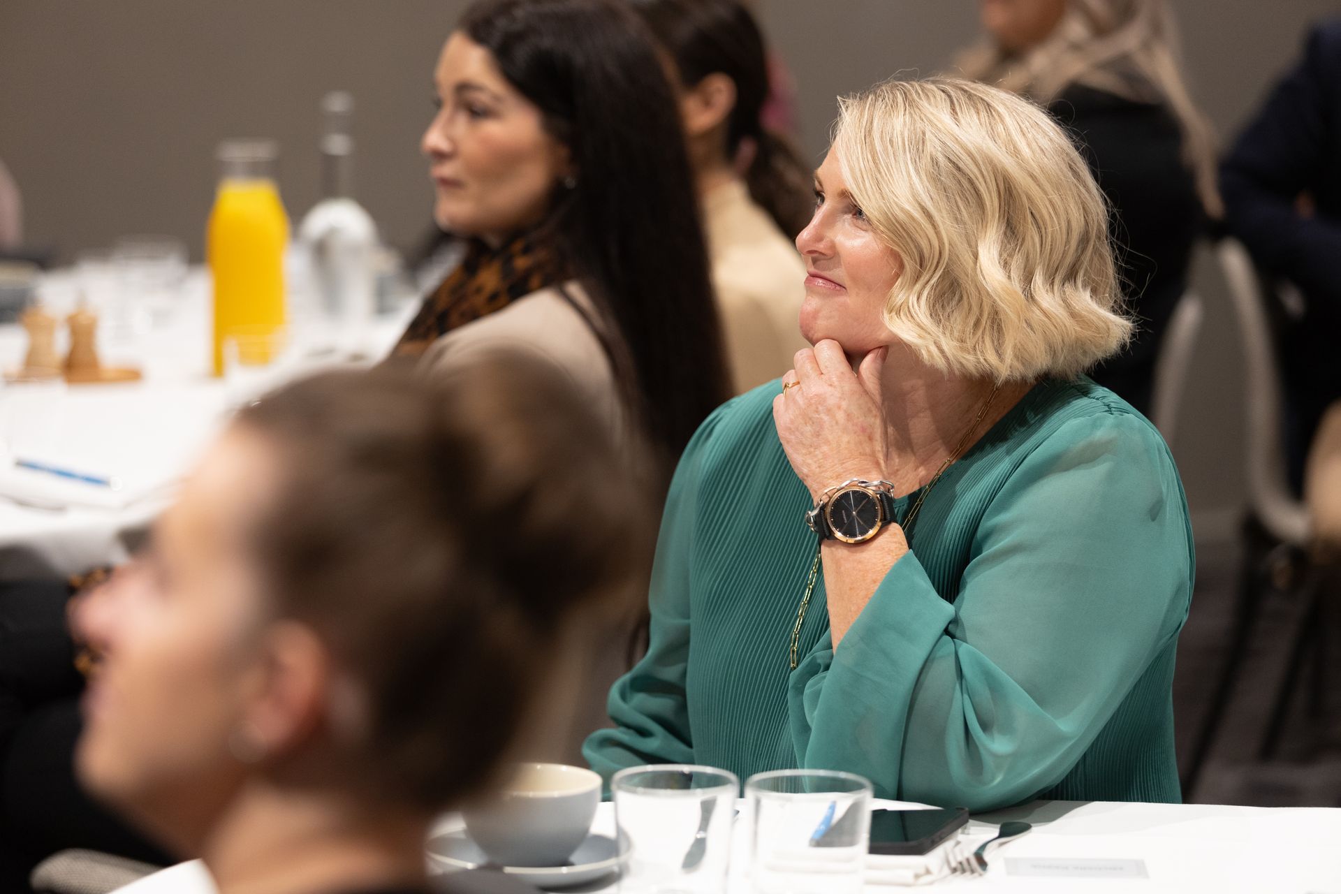 A woman in a green shirt is sitting at a table with other people.