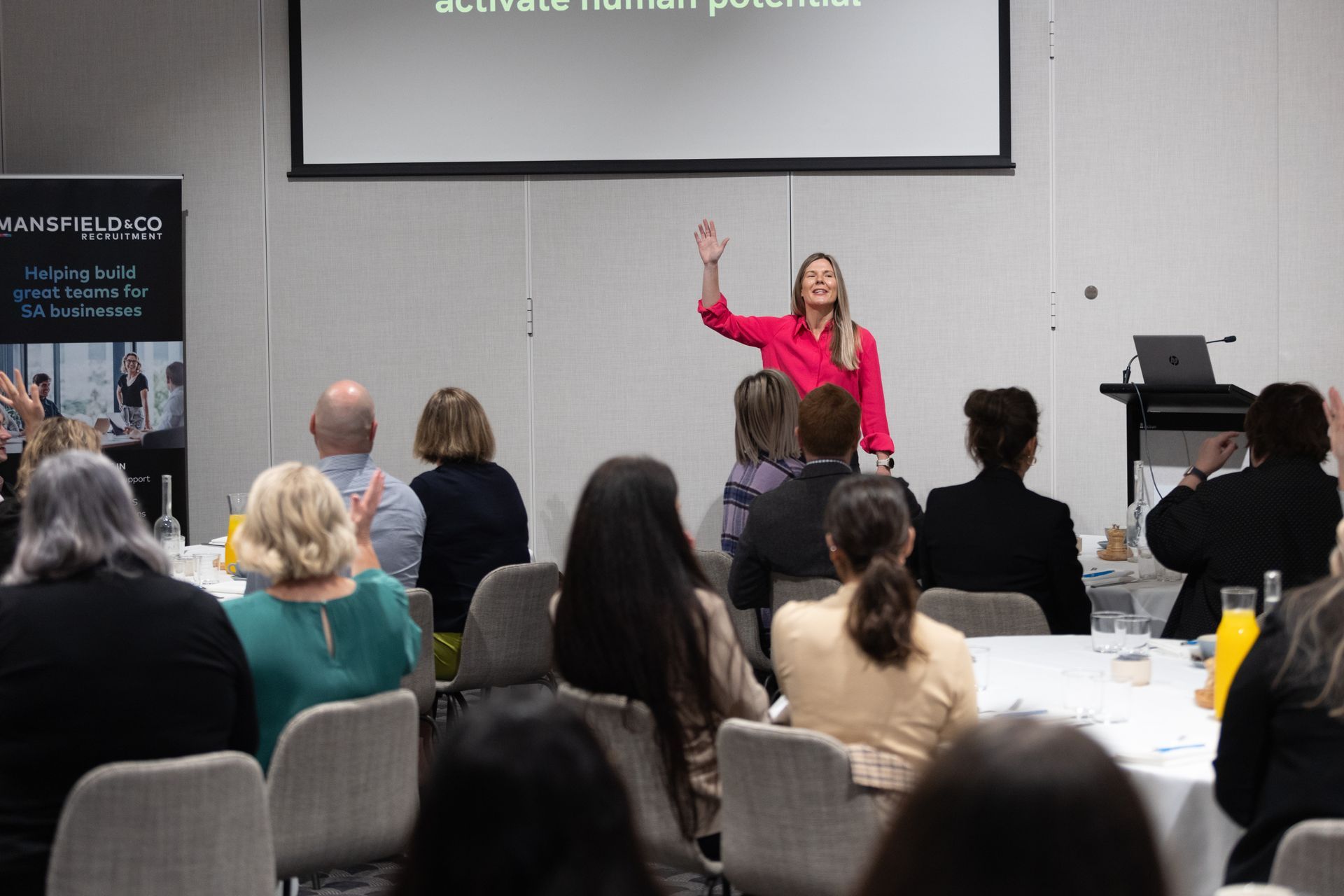 A woman is giving a presentation to a group of people sitting at tables.