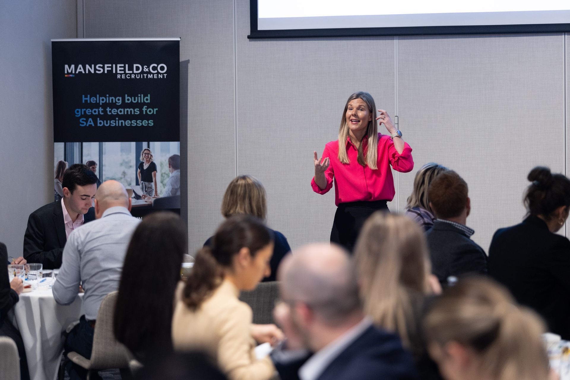 A woman is giving a presentation to a group of people sitting at tables.