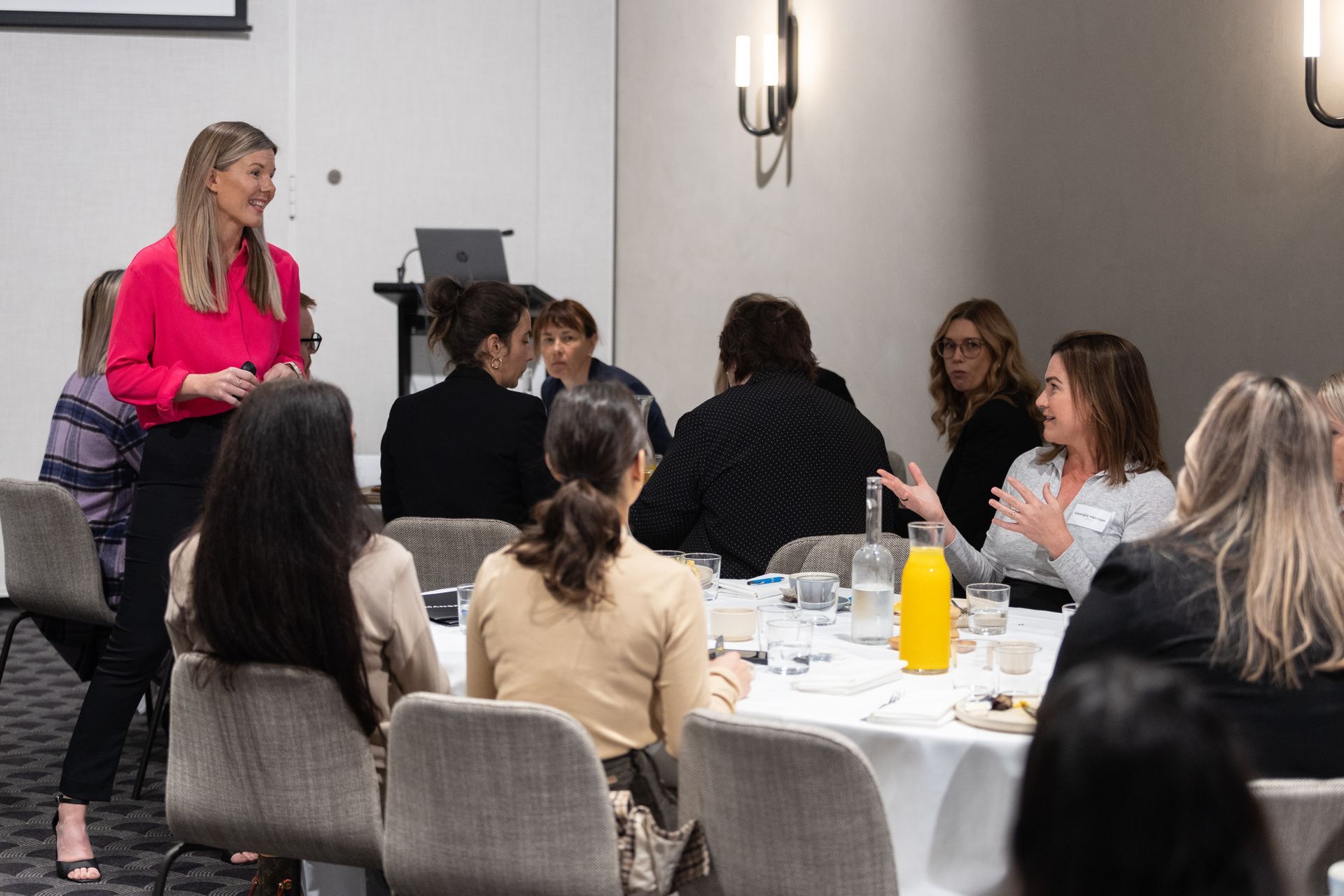 A woman is giving a presentation to a group of women sitting at tables.