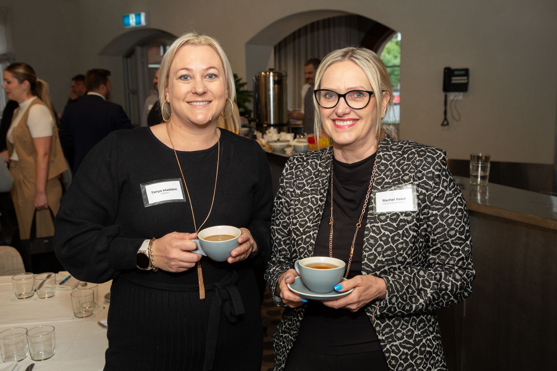Two women are standing next to each other holding cups of coffee.