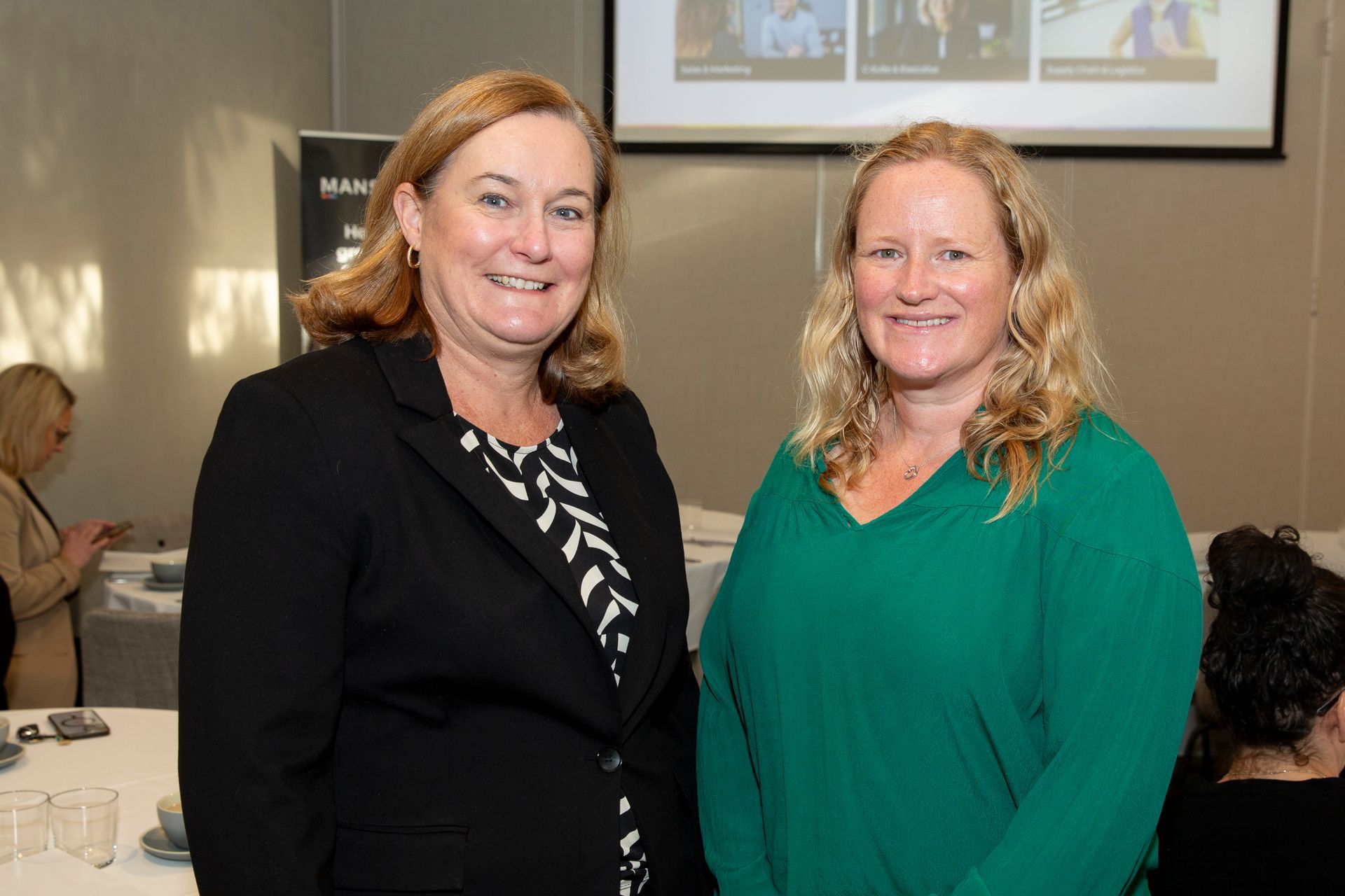 Two women are standing next to each other in front of a projector screen.