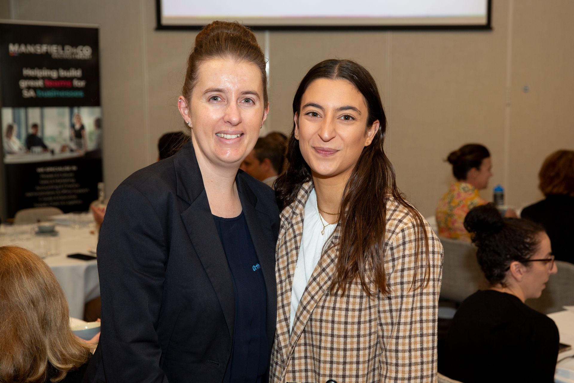 Two women are posing for a picture together at a conference.
