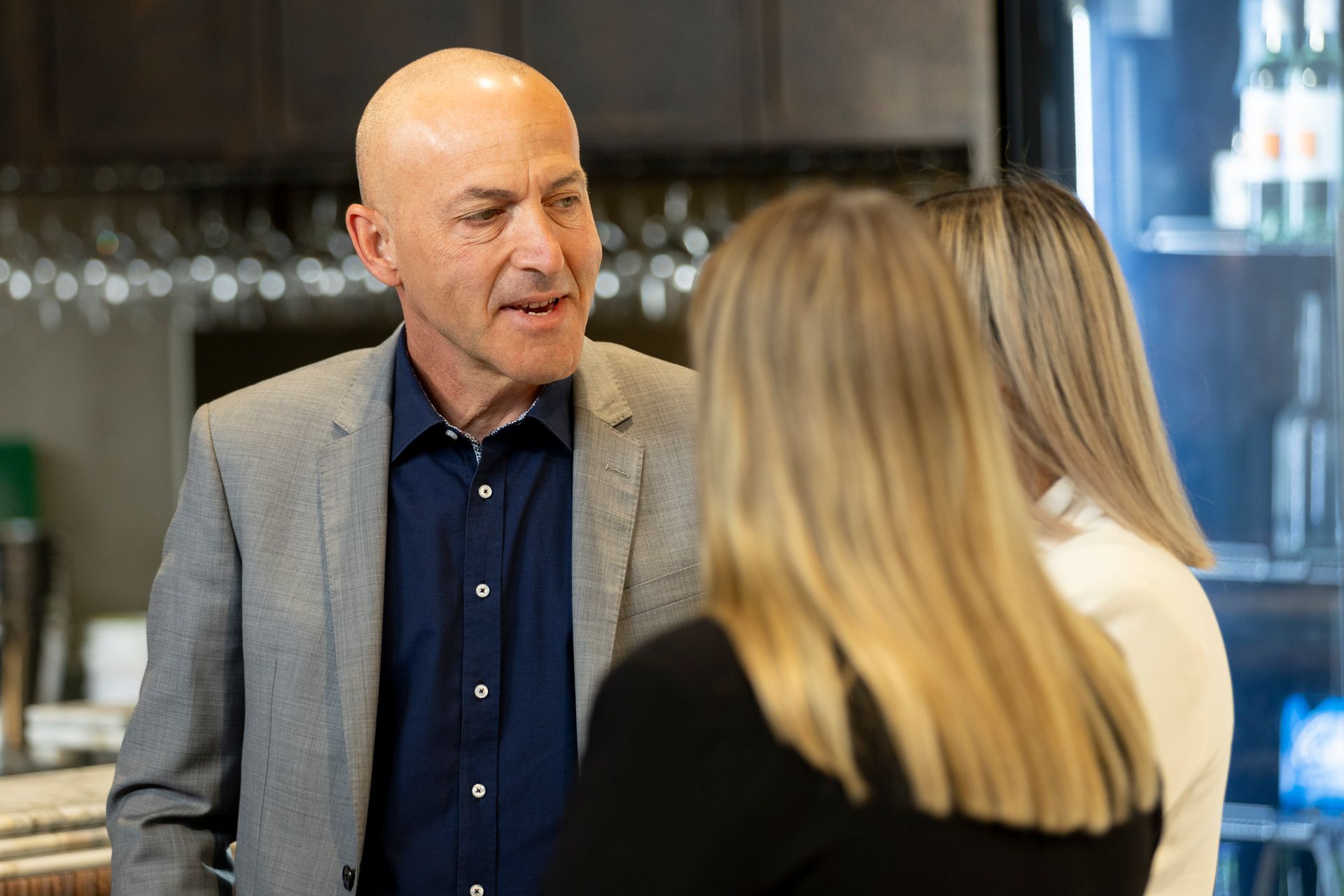 A man in a suit is talking to two women in a kitchen.