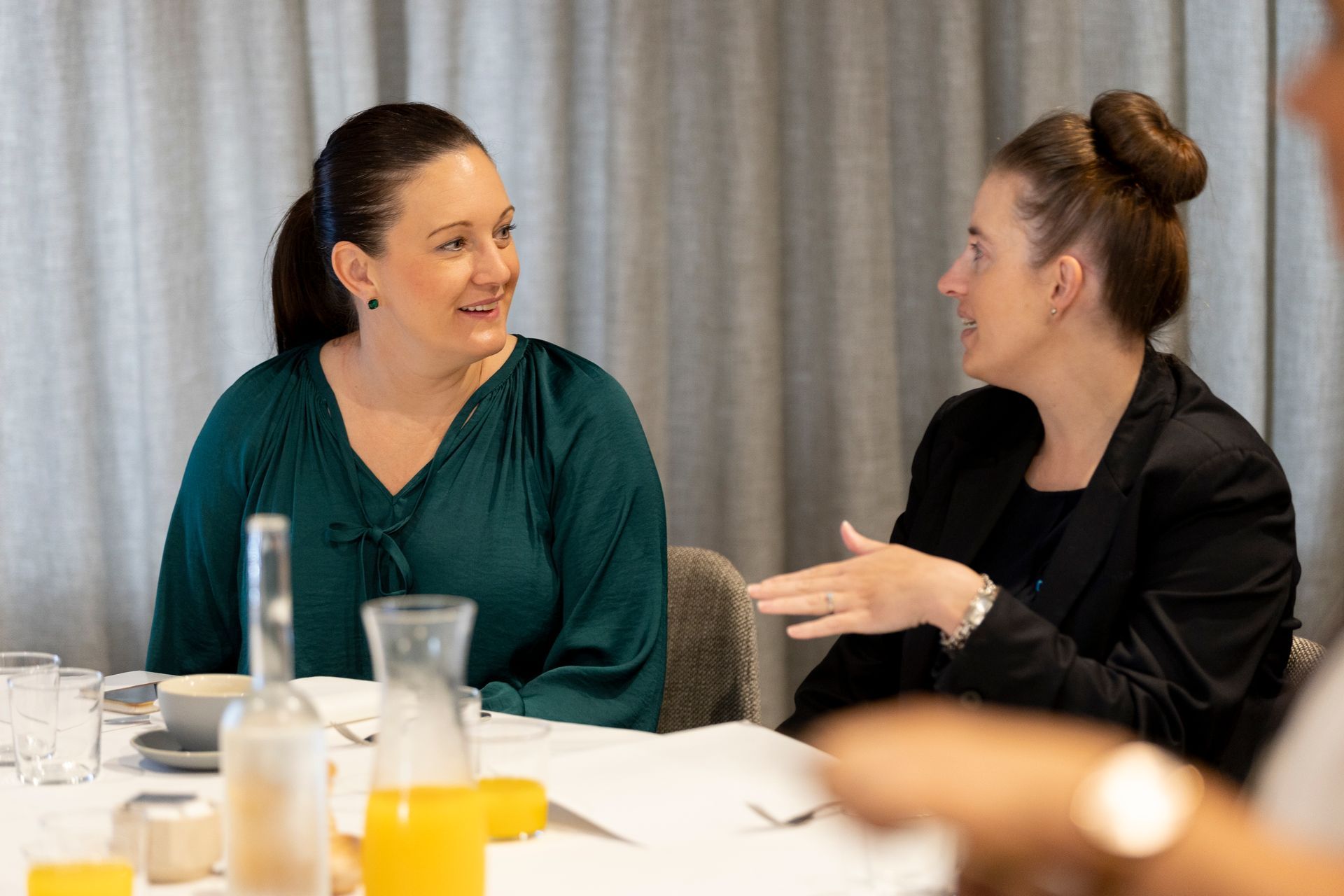 Two women are sitting at a table talking to each other.