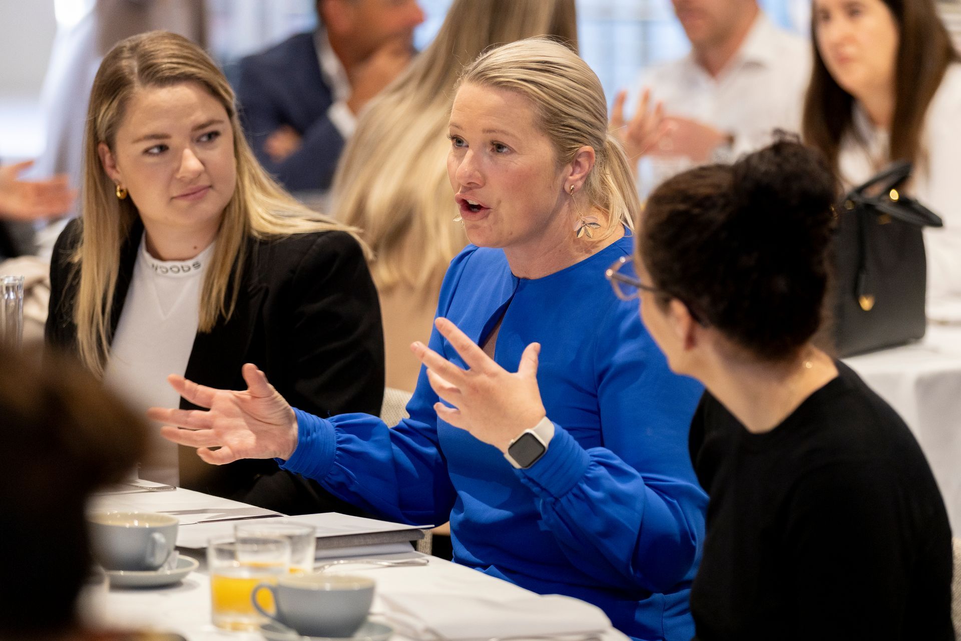 A group of women are sitting at a table talking to each other.