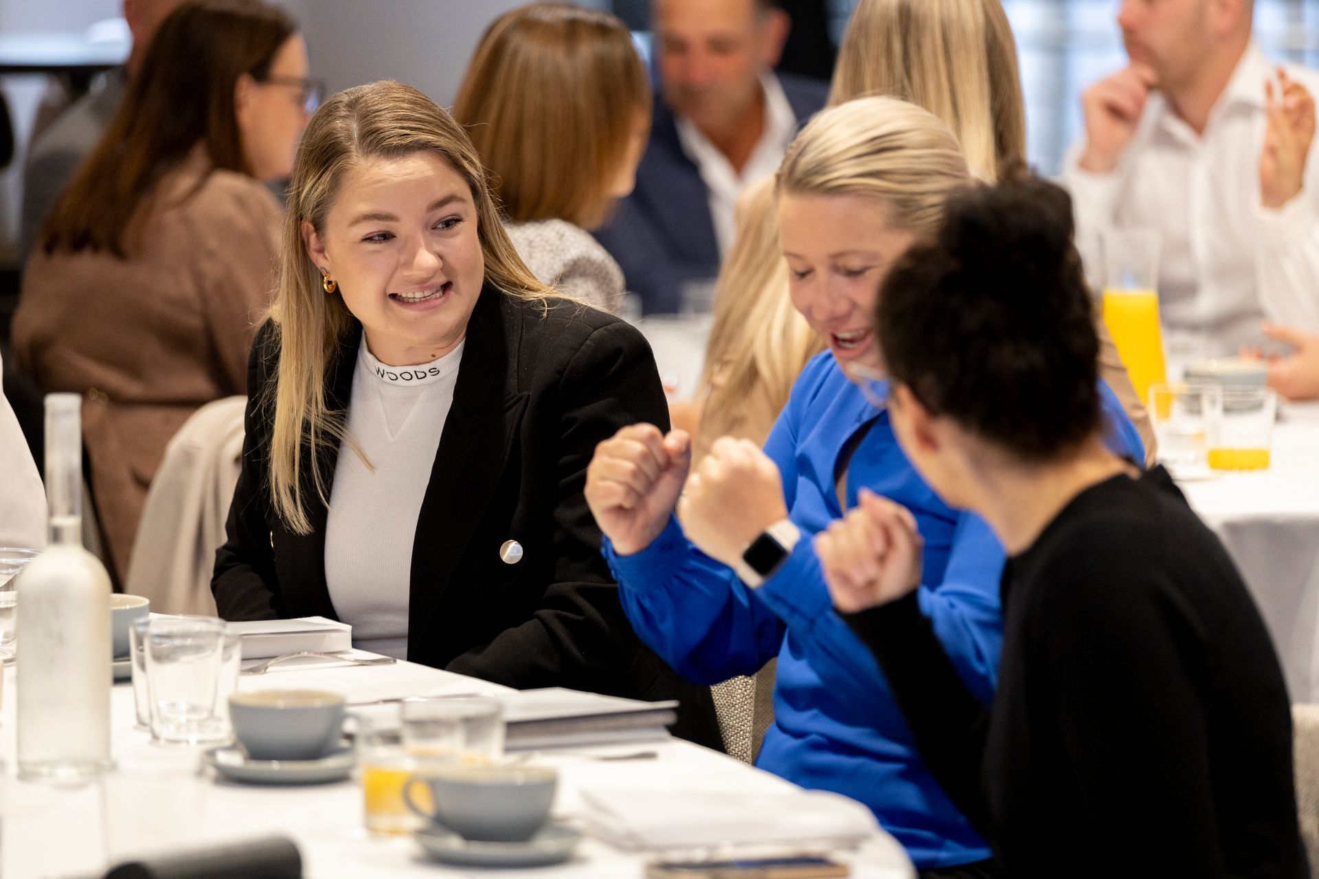 A group of people are sitting at a table with their hands in the air.