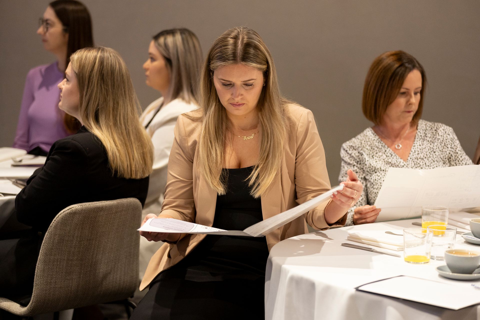 A group of women are sitting at tables looking at papers.