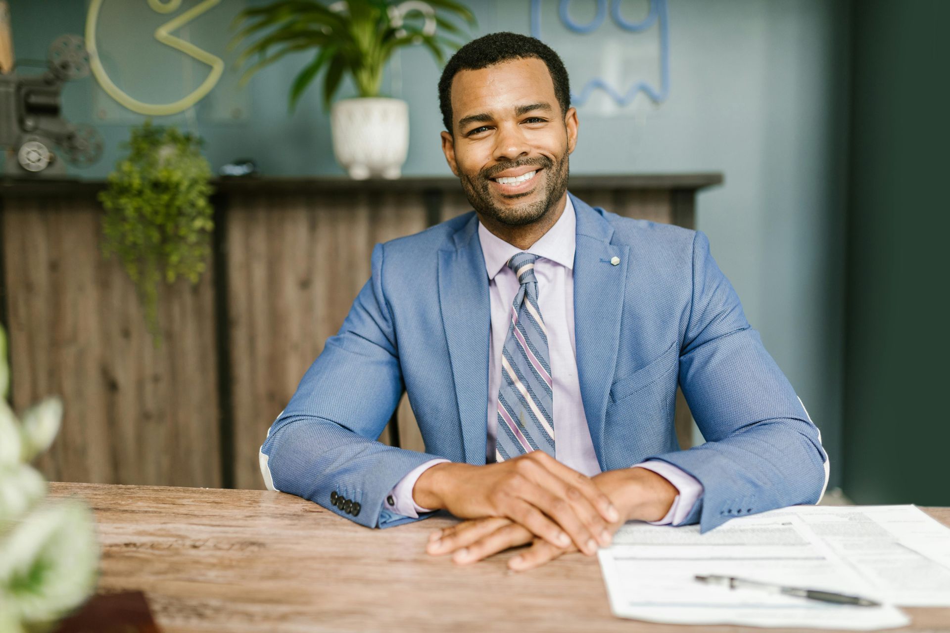 A man in a suit and tie is sitting at a desk with his hands folded.