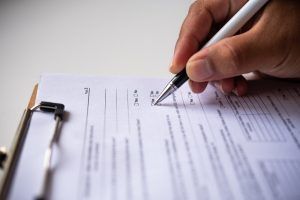 A person is writing on a clipboard with a pen.