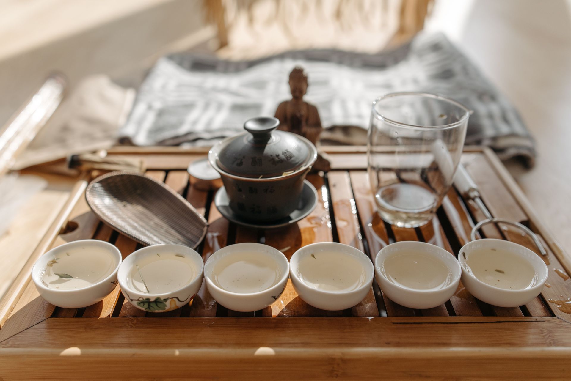 Gaiwan pouring Chinese green tea into a small cup on a bamboo tea tray — Adhara Tea & Botanicals