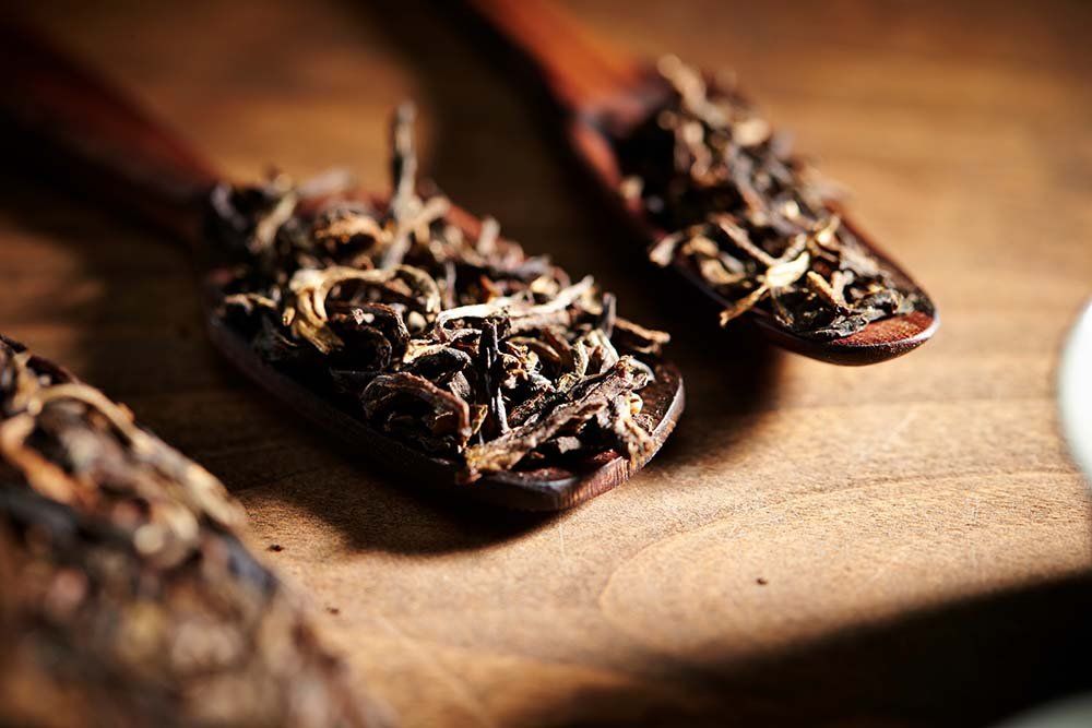 Three wooden spoons filled with tea leaves on a wooden table.