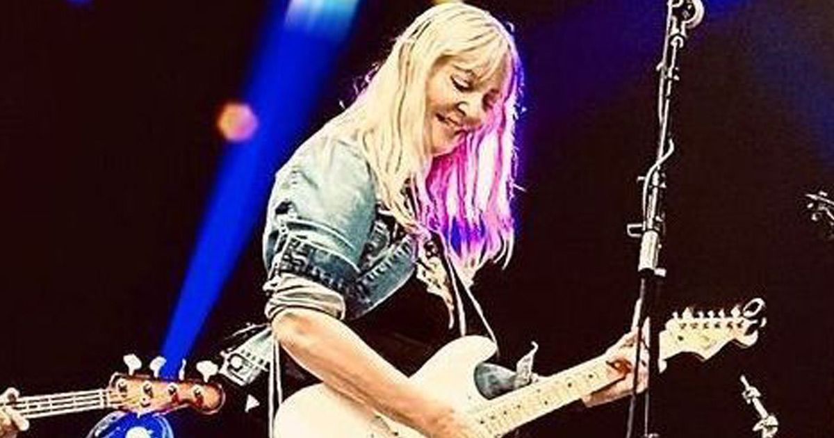 Linda Viens playing guitar on a stage in front of a microphone.