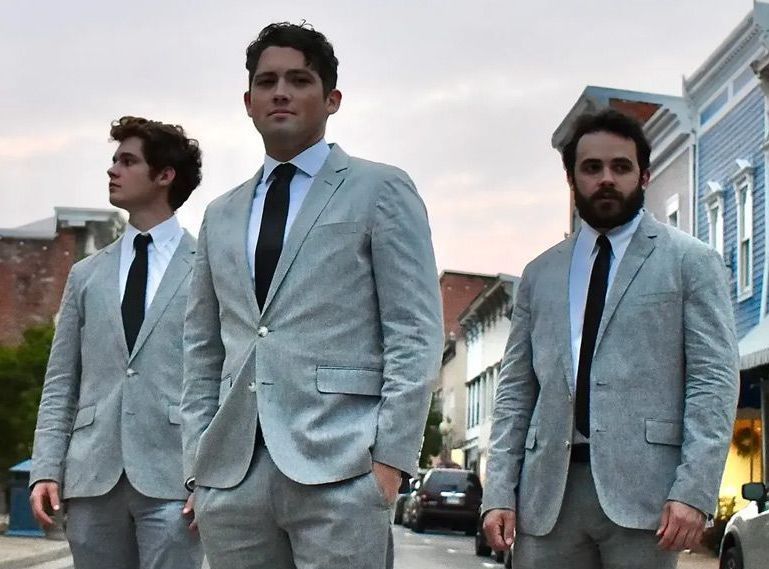 Three men in suits and ties are standing on a street